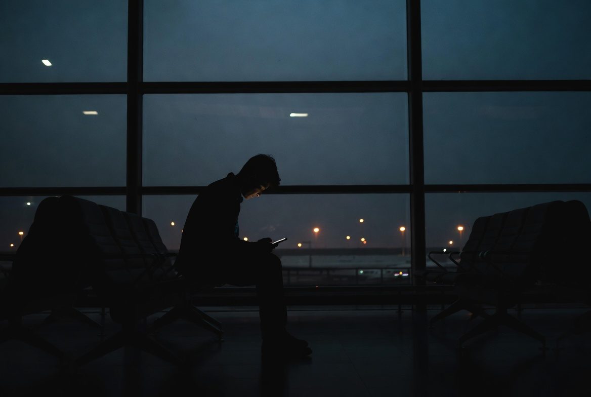 A lone traveler sitting in a dark airport gate at night, looking at their phone